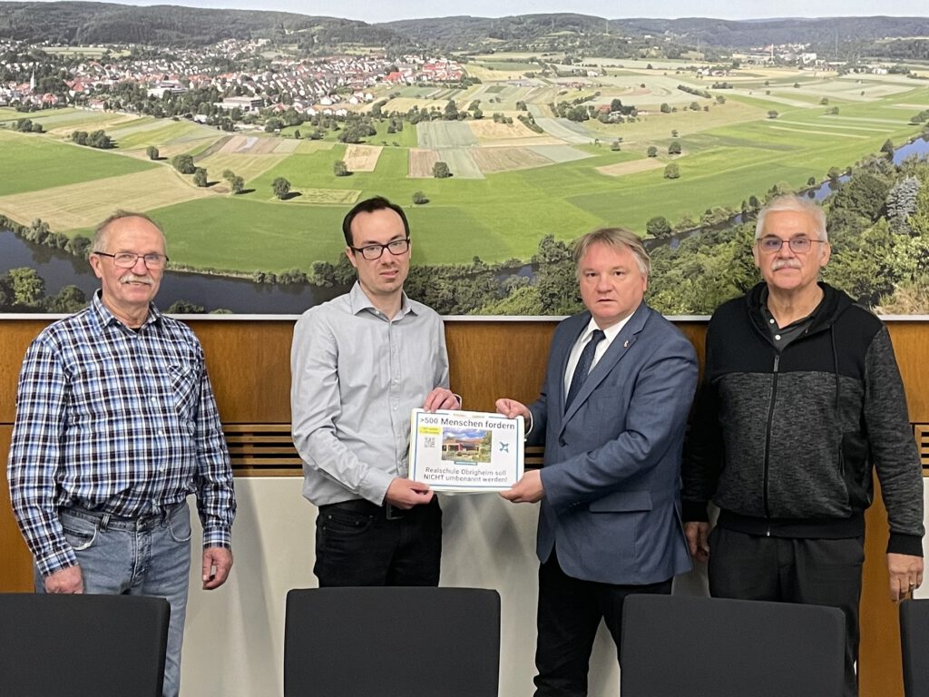 Vier Personen im Sitzungssaal des Rathauses in Obrigheim bei der Übergabe einer Petition für den Erhalt des Schulnamens der Realschule Obrigkeit. Frank Heuß (2.v.l.) übergibt die Unterlagen an Bürgermeister Achim Walter (2.v.r.). Alle schauen in die Kamera (Archivaufnahme).